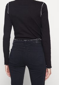 Svart långärmad topp med ribbad struktur, med en vågig nederkant och vit sömnad, kombinerad med mörkblå jeans med bakfickor.