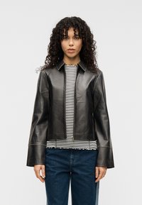 Μαύρο δερμάτινο μπουφάν με γιακά και κλείσιμο με φερμουάρ. Διαθέτει μανίκια σε σχήμα καμπάνας και ραφές με λεπτομέρειες. Φορεμένο πάνω από ριγέ τοπ.