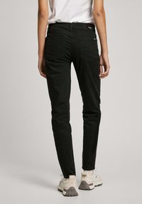 Crne slim-fit hlače od mješavine pamuka, s dva stražnja džepa i teksturiranom završnom obradom, uparene s svijetlim sportskim tenisicama.