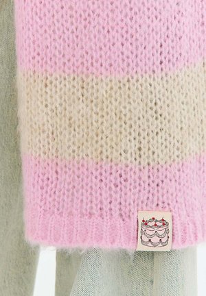 Miękki dziergany szalik z szerokimi różowymi i beżowymi paskami, z małą metką z ilustracją ciasta w kolorze czerwonym i czarnym.