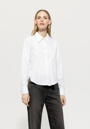 White collared shirt made of cotton with a button closure and long sleeves; paired with dark denim pants, featuring a relaxed fit.
