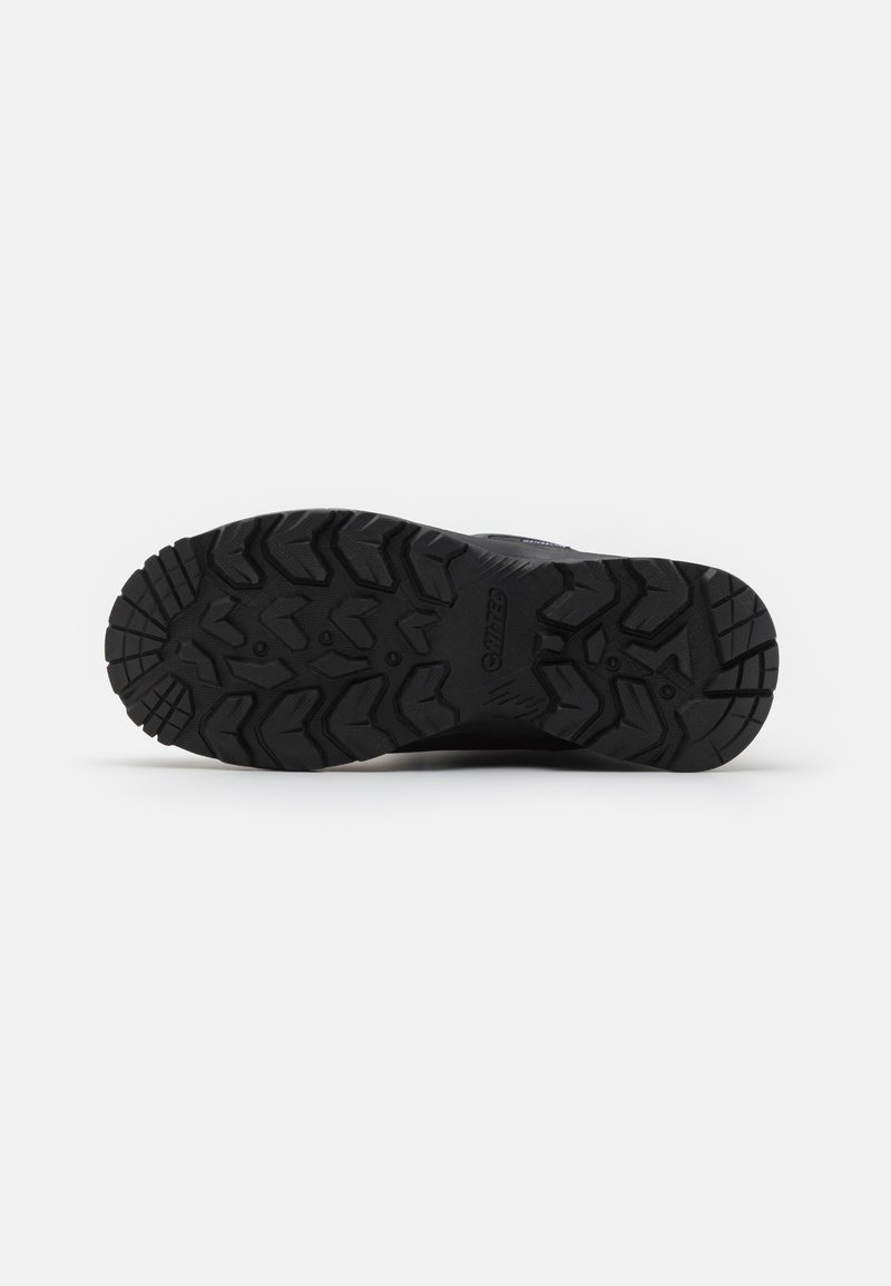 Suela de zapato de goma negra con patrones de surcos profundos y agresivos. Superficie texturizada, con acentos elevados para mejorar el agarre y el soporte.