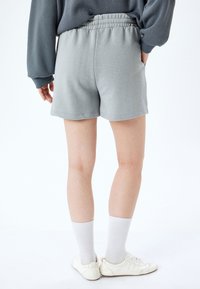 Shorts in cotone grigio chiaro con vita elastica, mostrati da dietro. Il tessuto è liscio e ha una silhouette informale.