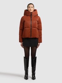 Brązowa puchowa kurtka z wysokim kołnierzem, zamkiem z przodu, elastycznymi mankietami i dwoma przednimi kieszeniami, zestawiona z czarną spódnicą i wysokimi czarnymi kozakami.