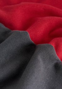 Cotton blend fabric featuring a subtle texture, with overlapping sections in dark gray and vibrant red, creating a dynamic visual contrast.