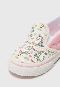 Canvas instapschoen in crème met een eenhoorn- en regenboogpatroon. Heeft een witte rubberen zool en een lichtroze interieur.