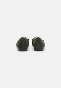 Scarpe slip-on in suede verde con punta arrotondata, dotate di una suola nera bassa e dettagli dorati sui lati.