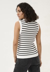Sleeveless striped top with black and white ribbed texture, featuring a fitted design and a rounded neckline, paired with dark pants.