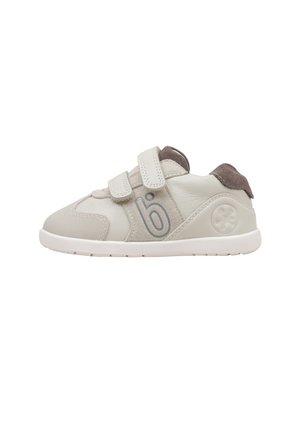 Zapatilla infantil de color beige claro con doble tira de velcro, detalles en ante gris y un logo de flor en el talón.