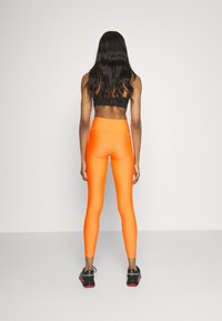 Leggings sportivi arancioni luminosi con una texture liscia e elastica e una vita alta, abbinati a un reggiseno sportivo nero e scarpe da ginnastica.