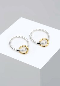 Boucles d'oreilles en argent avec une finition lisse, présentant un petit accent en or sous forme de cercle entrelacé avec l'anneau.