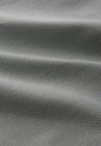 Tissu gris avec un petit motif en grille texturé et des plis doux créant des ombres et des reflets délicats.