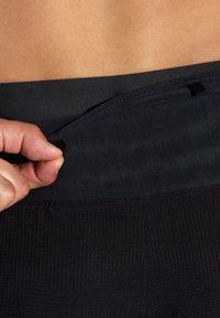 Zwarte sportleggings met een textuurpatroon; close-up geeft een hand weer die de tailleband aanpast en een minimalistisch ontwerp toont.