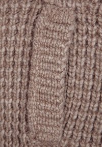 Tessuto lavorato a maglia beige con una texture a coste; presenta una sezione prominente e rialzata accentuata dal motivo di cucitura.