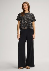 Kroppsnära svart topp med ett texturerat leopardmönster; kombinerad med lösa svarta byxor med en röd logotyp. Platta sandaler fulländar looken.