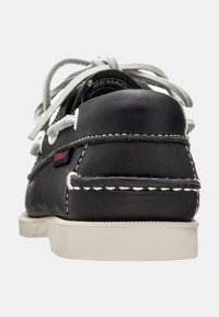 Zapato náutico de cuero negro con costuras blancas, cordones grises y un talón texturizado. La suela es de un color blanco roto con un diseño plano.