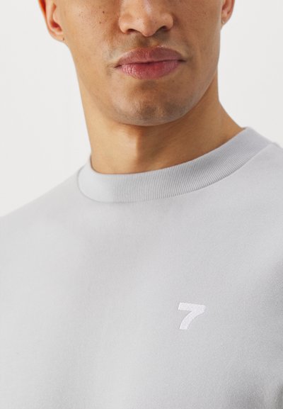 Sudadera gris claro con cuello redondo acanalado, textura suave y un pequeño '7' blanco bordado en el pecho.