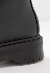 Stivale alla caviglia in pelle nera con suola in gomma testurizzata, caratterizzato da una finitura liscia, forma sagomata e dettagli cuciti lungo il bordo.