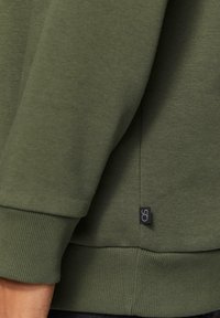 Grüne Sweatshirt mit gerippten Bündchen und Saum, strukturiertem Stoff und einem kleinen Logotag an der Seitennaht. Einfaches Design, geeignet für lässige Kleidung.