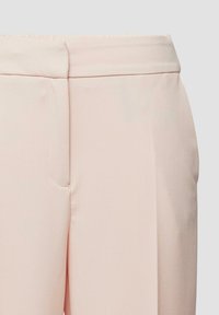 Close-up van lichtroze op maat gemaakte broek met een platte tailleband en verborgen frontsluiting.