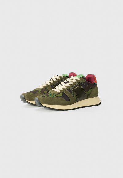 Grüne und schwarze Sportschuhe mit Camouflage-Muster, cremefarbenen Schnürsenkeln sowie roten und mintfarbenen Akzenten an Ferse und Zunge.