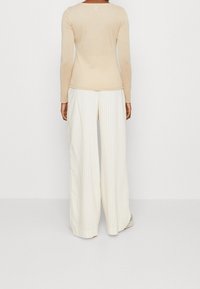 Haut beige à manches longues avec un design ajusté, associé à un pantalon large crème avec des rayures verticales et une texture lisse.