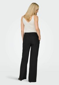 Črne hlače z elastičnim pasom in sproščenim krojem, kombinirane z belo, rebrasto, brezrokavno majico z izrezom v obliki črke V.