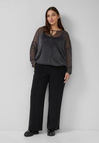 Schwarze Hosen mit weitem Bein, kombiniert mit einem metallisch schimmernden, dunklen, transparenten Oberteil mit rundem Ausschnitt und einer gebundenen Akzentuierung vorne.