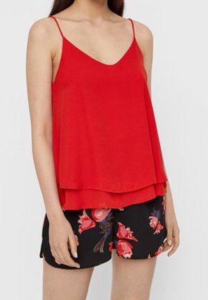 Femme portant un haut rouge sans manches ample avec de fines bretelles et un short noir à motif floral rouge.