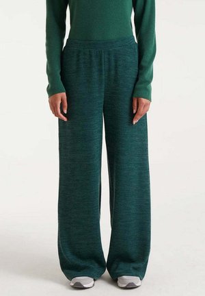 Pantalones de punto verdes de pierna ancha con un acabado texturizado y cintura elástica, combinados con una parte superior a juego y zapatillas grises.