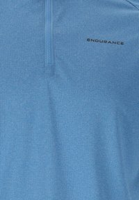 Sininen urheilupaita, jossa on lyhyt vetoketju kauluksessa ja musta "ENDURANCE"-teksti yläosassa rinnassa.