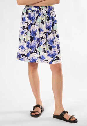 Blumiger Rock mit blauen, grünen und schwarzen Mustern, mit einem gerafften elastischen Bund, knielang, kombiniert mit flachen schwarzen Sandalen.