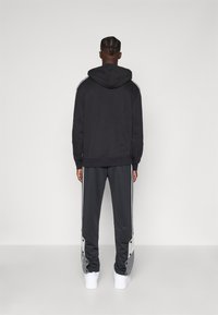 Mustat hupparit, joissa on harmaita yksityiskohtia, yhdistettynä harmaisiin collegehousuihin, joissa on nepparit ja valkoiset sivuraidat.