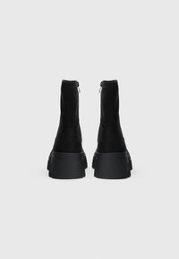 Črni gležnjarji z gladko teksturo, podplatom na platformo in zadnjimi zadrgami, s prefinjeno silhueto in minimalističnim dizajnom.