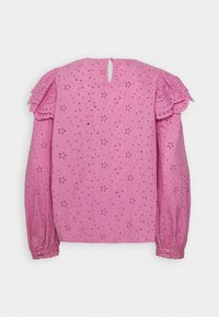 Blouse rose à manches longues avec broderie florale en œillet, détails froncés aux épaules, poignets boutonnés et petite ouverture en forme de trou de serrure au dos avec bouton.