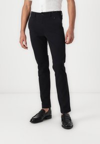 Black tailored trousers made of cotton blend, featuring a smooth texture, slim fit, and standard pocket design. Worn with black loafers.