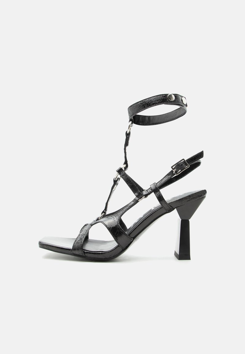 Μαύρο σανδάλι με λουράκια, τακούνι με τετράγωνη μύτη, λουράκι στον αστράγαλο με κουμπιά και γεωμετρικό στερεό τακούνι σε απλό λευκό φόντο.
