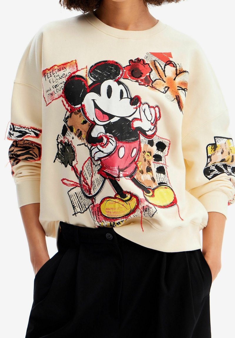 Felpa color crema con una grande grafica di Topolino in pantaloni rossi, con motivi floreali e dettagli in tecniche miste sulle maniche.