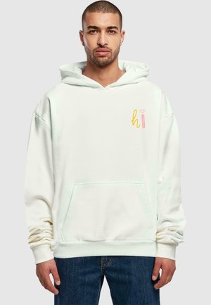 Light beige hoodie with a front pocket, drawstring hood, and text design in yellow and pink. Made from soft fabric with a relaxed fit.