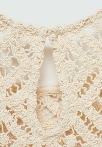 Crochet top in light beige, featuring an intricate lace pattern with a keyhole opening at the back and a soft, textured finish.