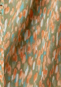 Tissu doux avec des taches abstraites en orange, turquoise, blanc et vert olive, créant un motif texturé et fluide.