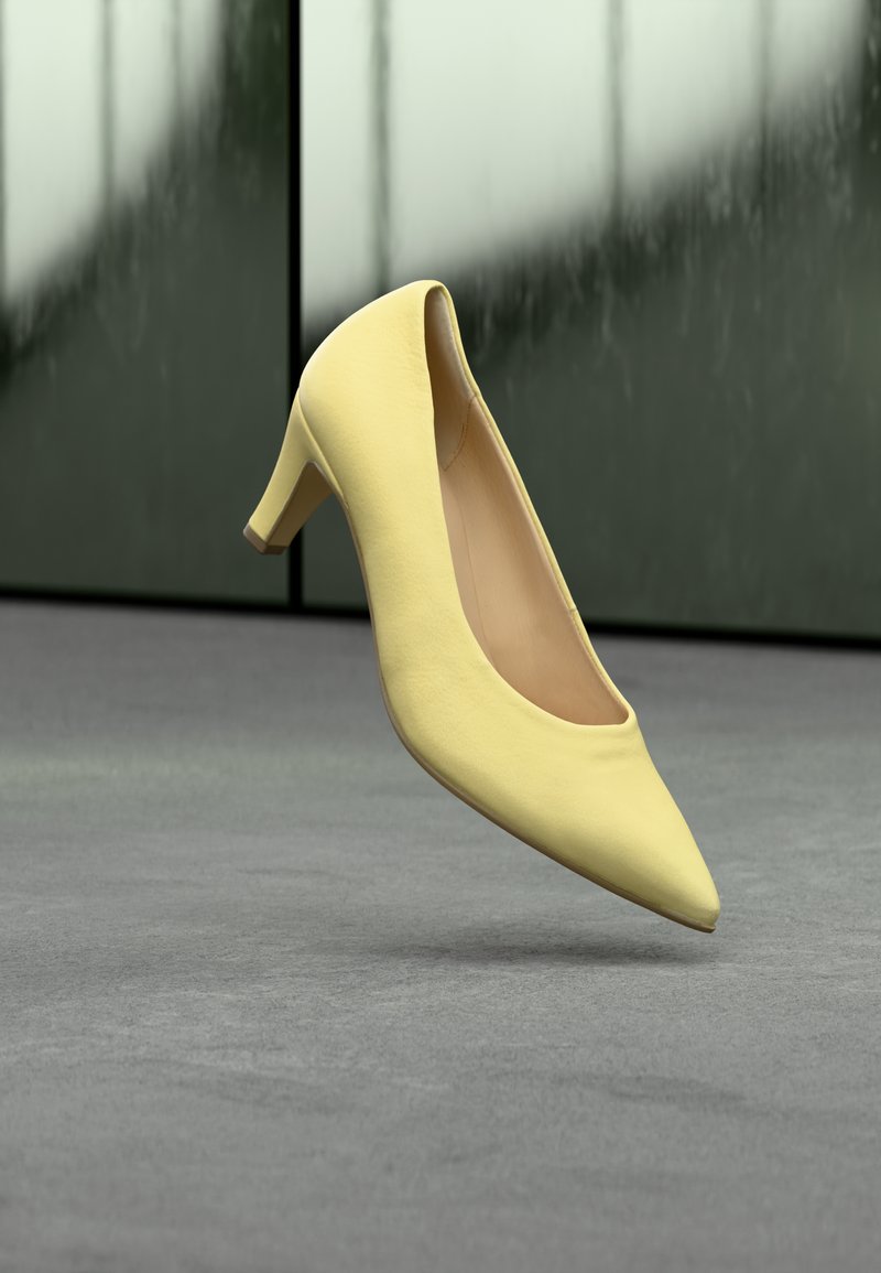 Talons en cuir jaune, bout pointu, talon bas et carré, texture lisse, design minimaliste, sur un fond gris avec une surface réfléchissante.