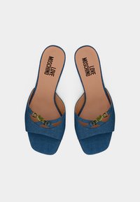 Μπλε τζιν σανδάλια ανοικτής φτέρνας, με μεταλλική λεπτομέρεια σε σχήμα καρδιάς «LOVE» σε χρυσό χρώμα στις διασταυρωμένες λουρίδες και ταμπά εσωτερική επένδυση με την επωνυμία «LOVE MOSCHINO».