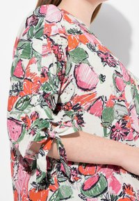 Blusa corta de manga corta colorida con estampados de frutas y flores. Confeccionada en tejido ligero, presenta detalles de lazo en las mangas.