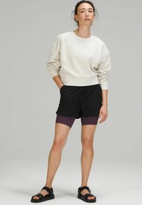 Crème sweatshirt, zwarte shorts, paarse fietsbroek eronder en zwarte sandalen. Heeft een relaxte pasvorm en een ronde halslijn.
