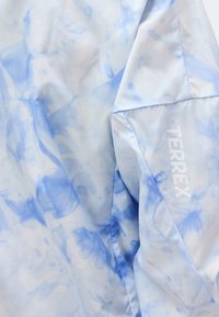 Υφασμάτινο tie-dye σε γαλάζιο και λευκό με ορατά ραφές και την επιγραφή "TERREX" με άσπρα γράμματα σε διπλωμένο τμήμα του υλικού.