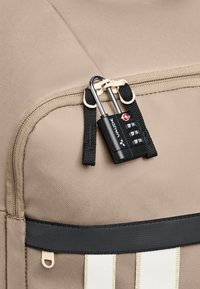 Beige stoffen tas met een rits, voorzien van een zwart cijferslot dat met banden is bevestigd. Inclusief een zwart-wit gestreepte accent.