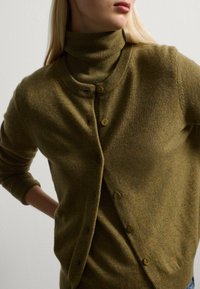 Cardigan lavorato a maglia verde oliva con collo alto, caratterizzato da bottoni marroni e una consistenza morbida. La vestibilità è rilassata con polsini a coste.