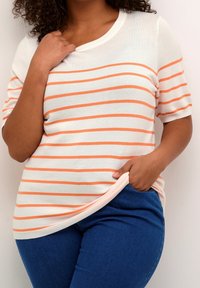 White striped t-shirt with orange stripes, short sleeves, ribbed neckline, and a relaxed fit, paired with blue denim jeans.
