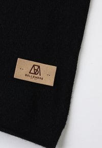 Sciarpa nera in maglia con etichetta in suede. L'etichetta presenta un logo impresso in marrone scuro, fissato con due cuciture. Texture morbida, design semplice.